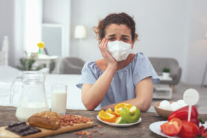 woman with a mask on sitting at a table covered in food items